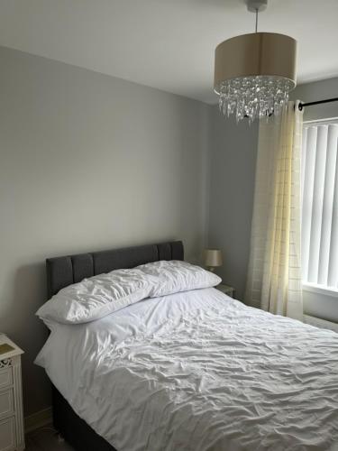 a bedroom with a bed with white sheets and a chandelier at Garden Avenue in Portstewart