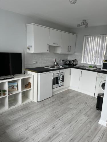 a kitchen with white cabinets and a tv in it at Garden Avenue in Portstewart