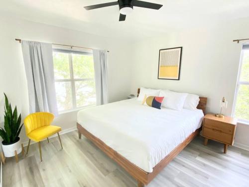 a white bedroom with a bed and a yellow chair at Sanctuary Gainesville Bright 2 BR King Condo in Gainesville