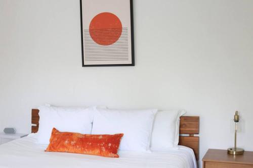a bed with white sheets and a orange pillow on it at Sanctuary Gainesville Bright 2 BR King Condo in Gainesville