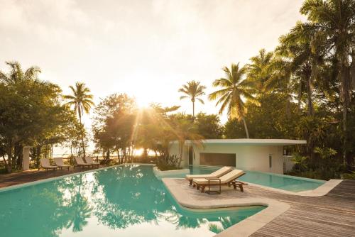 a pool with chairs and a house with palm trees at Auka Boipeba in Ilha de Boipeba