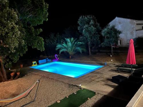 a swimming pool at night with a pink umbrella at Maison de vacances in Ventiseri