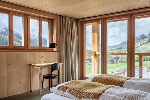 1 Schlafzimmer mit 2 Betten, einem Schreibtisch und Fenstern in der Unterkunft Berglodge Goms (Hotel) in Münster VS