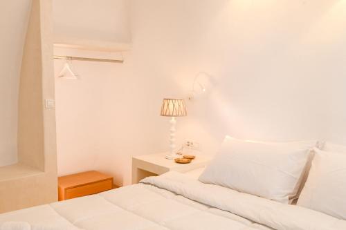 a white bedroom with a bed and a lamp at Three Bells Suites in Firostefani