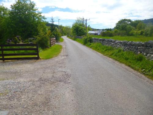 an empty road with a stone wall and a fence at Aslaich in Drumnadrochit