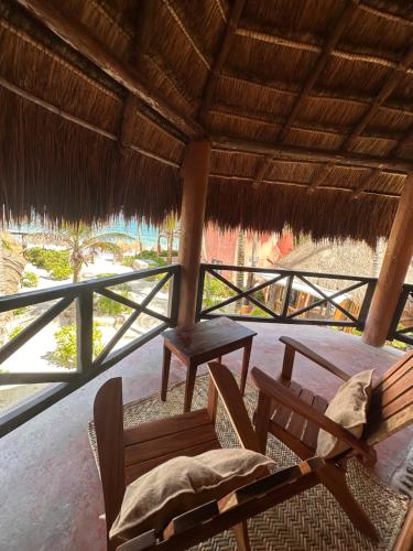 a porch with two chairs and a table and a straw roof at La Conchita Tulum in Tulum