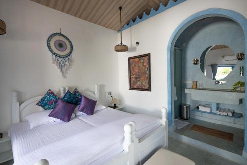 a bedroom with a white bed with purple and blue pillows at One At Goa in Canacona