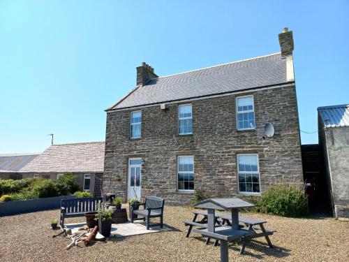 ein Backsteingebäude mit Picknicktischen und Bänken davor in der Unterkunft Orkney Retreats 1 2 and 3 bedroom Island Farmhouses & Cottages in Sanday