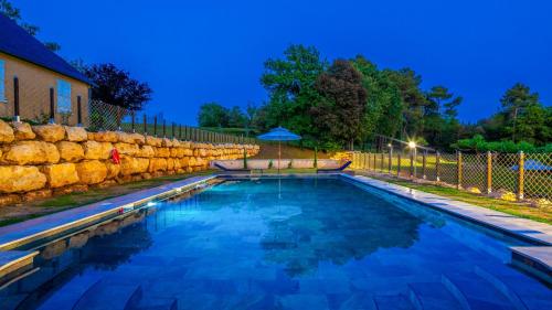 a swimming pool in a yard with a stone wall at Hameau du Château de Giverzac, gîtes luxueuses in Domme