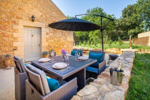 a patio with a table and chairs and an umbrella at Hameau du Château de Giverzac, gîtes luxueuses in Domme