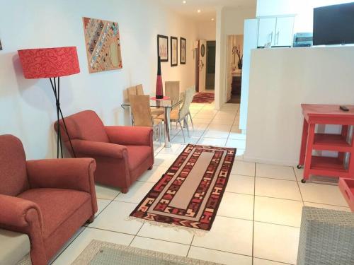 a living room with red chairs and a rug at Modern 2Bedroom Self Catering unit HBos. in Mossel Bay