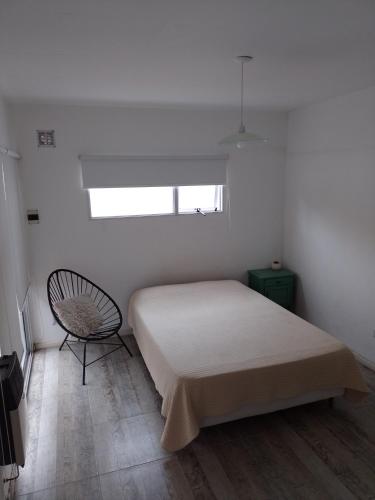 a white bedroom with a bed and a chair at Aires de mar in San Clemente del Tuyú