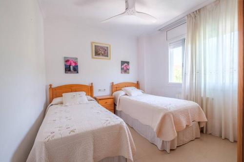 two beds in a white room with a window at Apartamento en complejo residencial, con piscina. in Salou