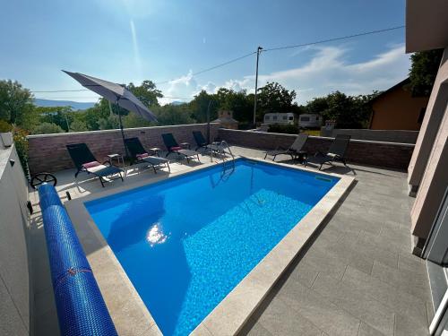 a swimming pool with chairs and an umbrella on a patio at Holiday house "Sabine pink" in Skrbčići