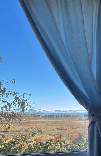 uma vista para um campo a partir de uma janela com uma cortina azul em CALAFATE WIFI Depto 2 personas em El Calafate