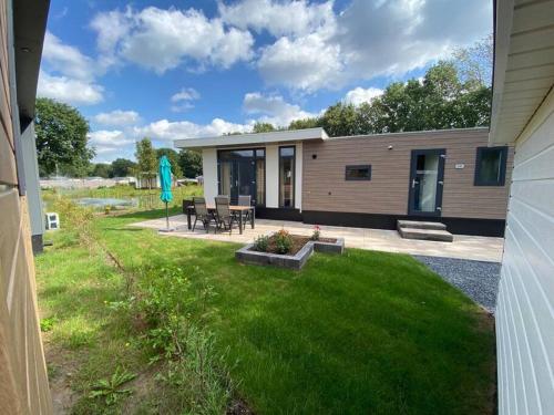 een klein huis met een patio en een grasveld bij Kindvriendelijk luxe chalet in de bossen met privé sauna in Harderwijk