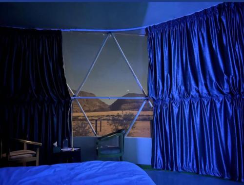 a bedroom with blue curtains and a bed and a window at Adel rum camp bubbles in Wadi Rum