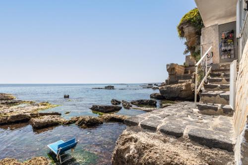 a blue bench sitting on the rocks next to the ocean at Giuggiulena in Siracusa