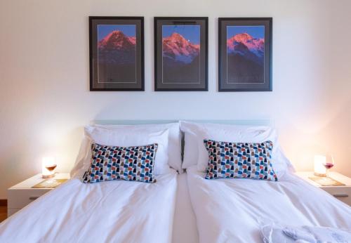 a bedroom with a white bed with three pictures on the wall at Chalet Bargsunna in Wengen