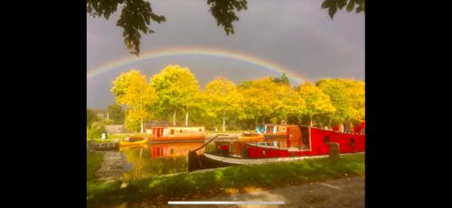 a rainbow in the sky over a river with boats at Très jolie péniche à louer in Hédé