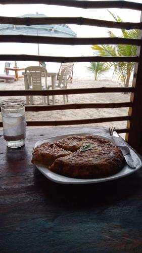 una pizza en un plato en una mesa con un vaso de agua en La Cabaña, en Montañita