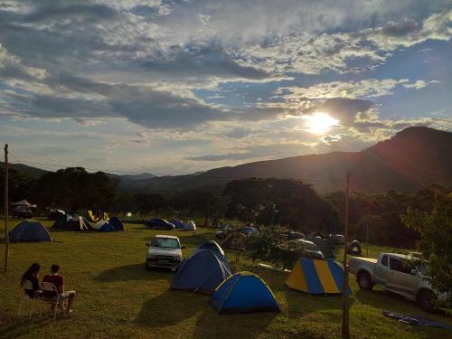 a group of tents in a field with the sun setting at camping toca raul in São Thomé das Letras