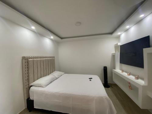 een witte slaapkamer met een bed en een televisie bij Hermoso apartamento a solo 15 minutos del parque del cafe in Montenegro