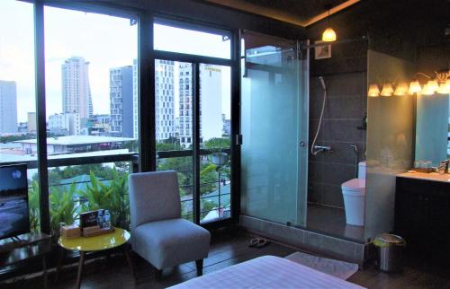 a bathroom with a shower and a chair with a view at Oasis Hotel & Apartment in Da Nang