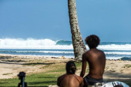 two people sitting on the beach looking at the ocean at Sumatra Surf Resort in Biha
