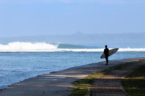 a man walking down a sidewalk with a surfboard at Sumatra Surf Resort in Biha