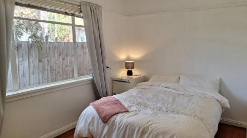 a white bedroom with a bed and a window at A cozy place in Noble Park