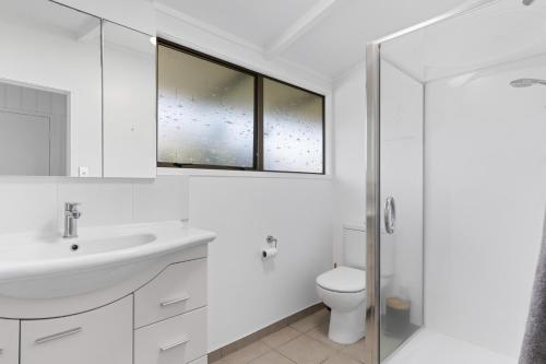 a white bathroom with a sink and a toilet at Pukehina Estuary Sunset Views Holiday Home in Pukehina