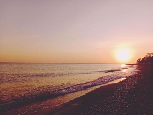 a beach with the sun setting over the water at Kumpul Beach in Amed