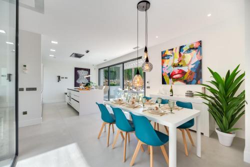 a kitchen and dining room with a white table and blue chairs at VACATION MARBELLA I Villa Chloe The Golfer, Infinity Pool, Rooftop Views, New-Built in Estepona