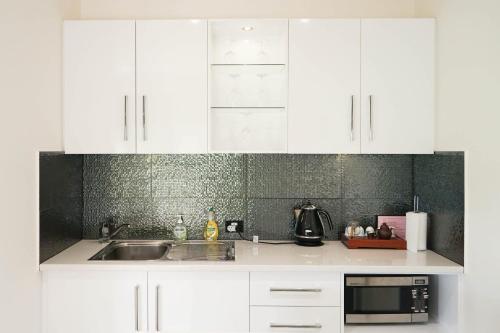a kitchen with white cabinets and a sink and a microwave at Petit Verdot Cottage - A Vineyard Retreat in Barossa Valley in Rowland Flat