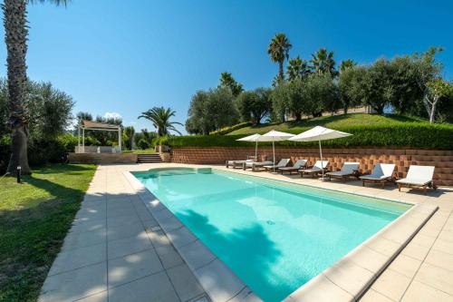 a swimming pool with chairs and umbrellas in a yard at Villa Iulia - VIBRA in Controguerra