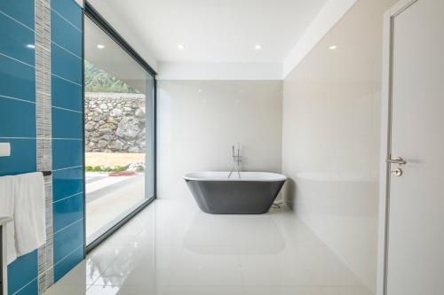 a bathroom with a tub and a glass door at Shell House by GALMI in Arco da Calheta