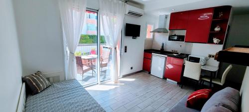 Elle comprend une petite cuisine avec des placards rouges et une porte donnant sur un balcon. dans l'établissement Rêve Azur studio 6 à deux pas de la mer Parking wifi, à Cagnes-sur-Mer