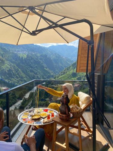 a woman sitting at a table under an umbrella at Valent Suit Bungalov in Ardeşen