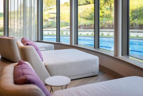 a living room with two chairs and a couch and windows at Heilthermen Resort Bad Waltersdorf in Bad Waltersdorf