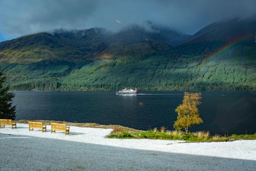 a boat in the water with two benches and a rainbow at Black Sheep Hotels Cabins in Spean Bridge