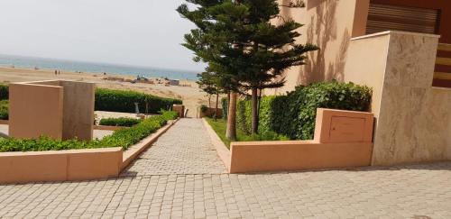 a sidewalk next to a building with a tree and the beach at Appartement pied dans l'eau in Imi Ouaddar