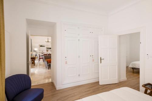 a white bedroom with white doors and a blue chair at PALACIO DON CARLOS in Jerez de la Frontera