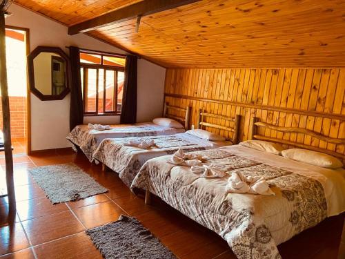 three beds in a room with wooden walls at Pousada Cantinho da Montanha in Visconde De Maua