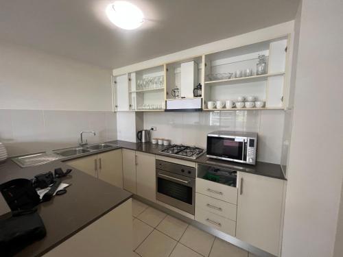 cocina con armarios blancos y microondas en Westmead Home away from home, en Westmead