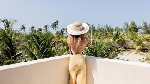 a woman in a hat standing on a balcony looking at palm trees at Avra Tatajuba in Tatajuba