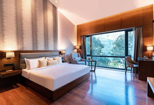 a bedroom with a large bed and a large window at The Rosefinch Sarovar Portico in Bhīm Tāl