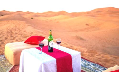 a table with a bottle of wine and two glasses at Holiday Desert Camp in Merzouga