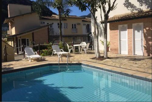 a pool with chairs and a table and a house at Casa em condominio na Praia de Juquehy in São Sebastião
