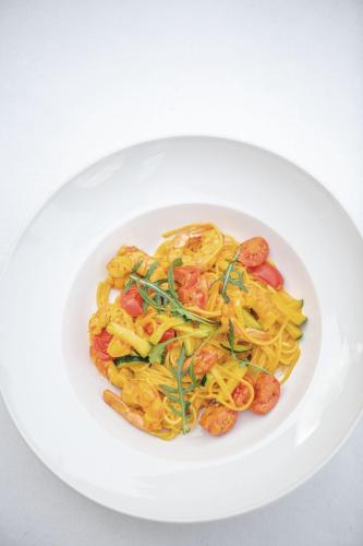 a white plate of pasta with shrimp and vegetables at Gasthof Teiser Stern in Funes